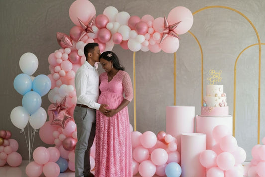Couple standing in front of a cake and balloon arch at a baby shower.