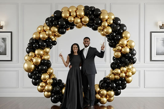 Man and woman posing in front of a 7' circle balloon arch with black and gold balloons for engagement photo