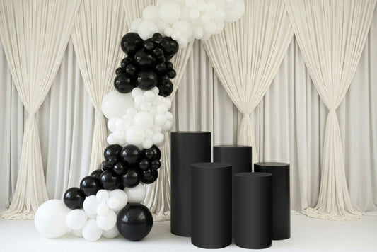 Black and white balloon arch with five piece pedestals against a white curtain backdrop