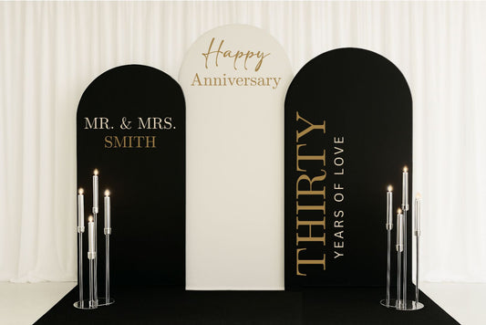 Decorative backdrop with 'Happy Anniversary' and 'Mr. & Mrs. Smith' text, featuring candles on a white background.