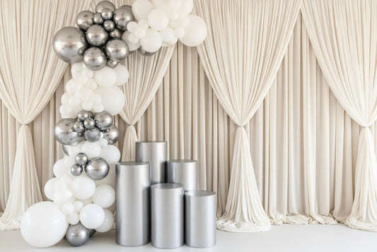 Decorative setup with silver and white balloons and five piece cake cylinders