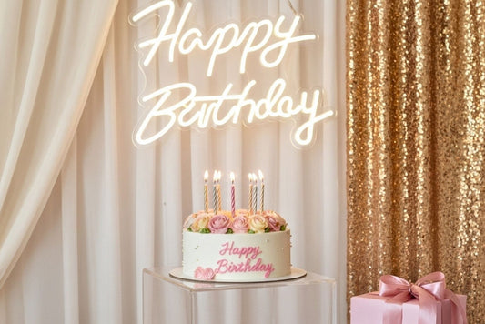 Happy Birthday Small Neon sign with a cake on a pedestal in front of beige & gold drapes.