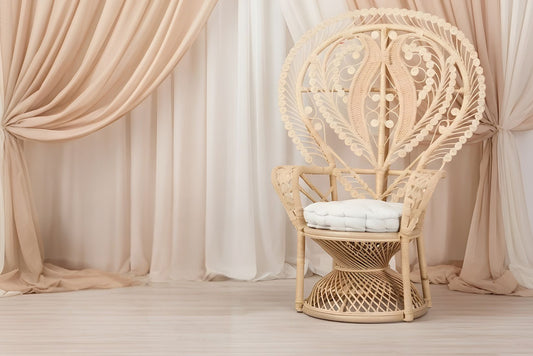 Wicker peacock chair with white cushion in a room with beige and white pipe and drape.