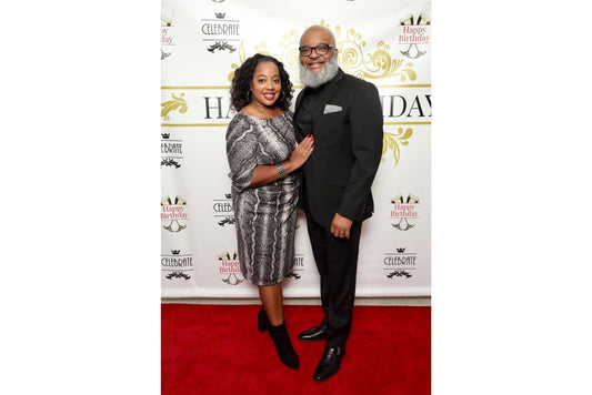 Two people posing on a red carpet event with a branded happy birthday backdrop