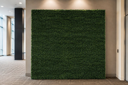 A large rectangular artificial green hedge wall mounted on a beige wall in an indoor office or hallway space with carpeted floor and recessed lighting.