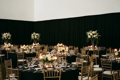 Black fabric background with gold wedding chairs and ivory cushions.