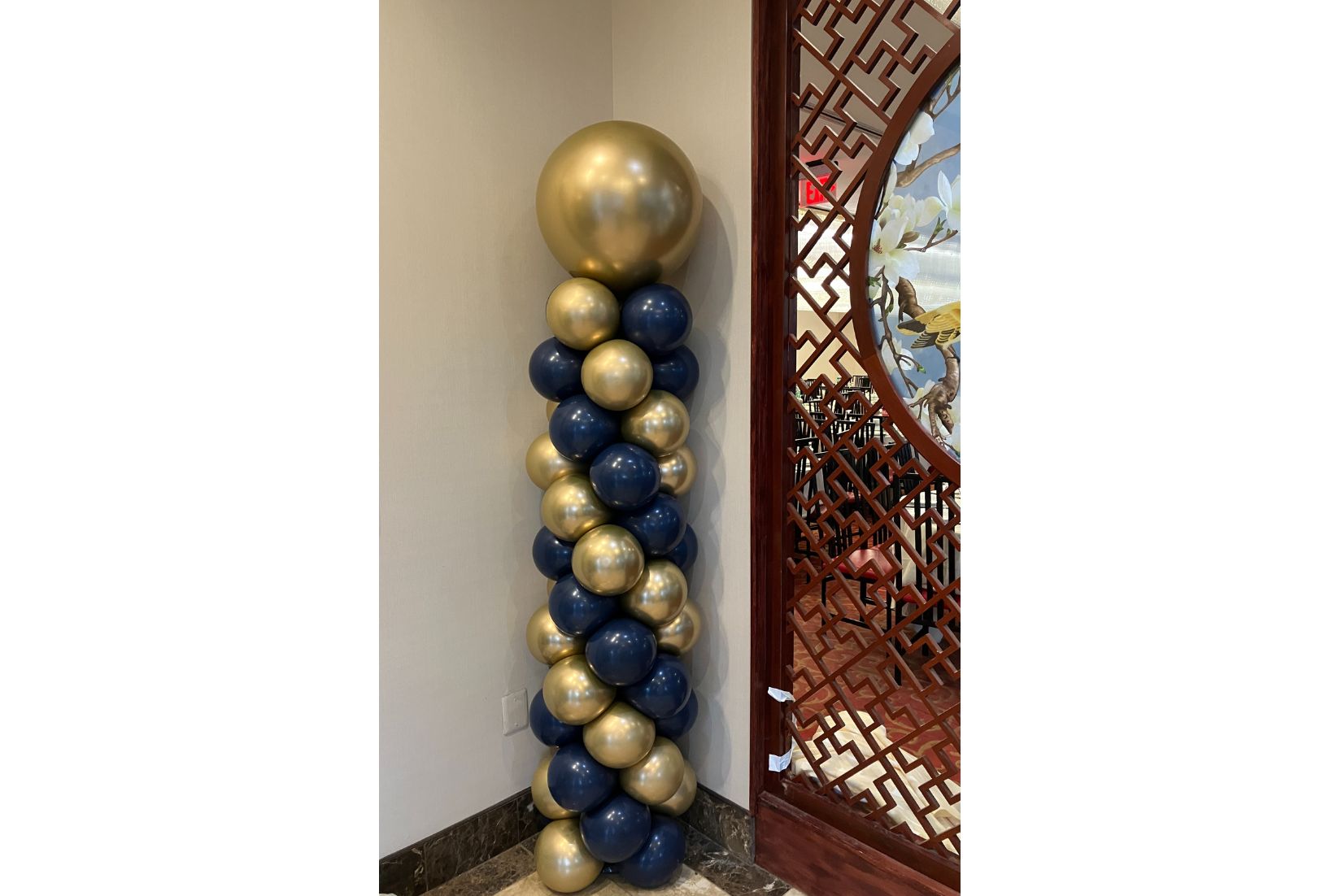 Decorative column of blue and gold balloons against a white wall.