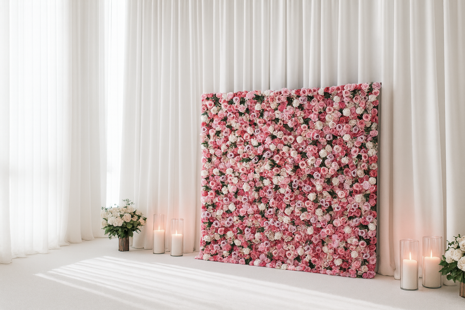 Floral wall backdrop with pink and white flowers in a room with white curtains and candles.