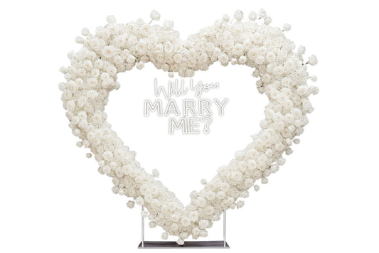Heart-shaped white rose backdrop with large 'Will You Marry Me?' neon sign
