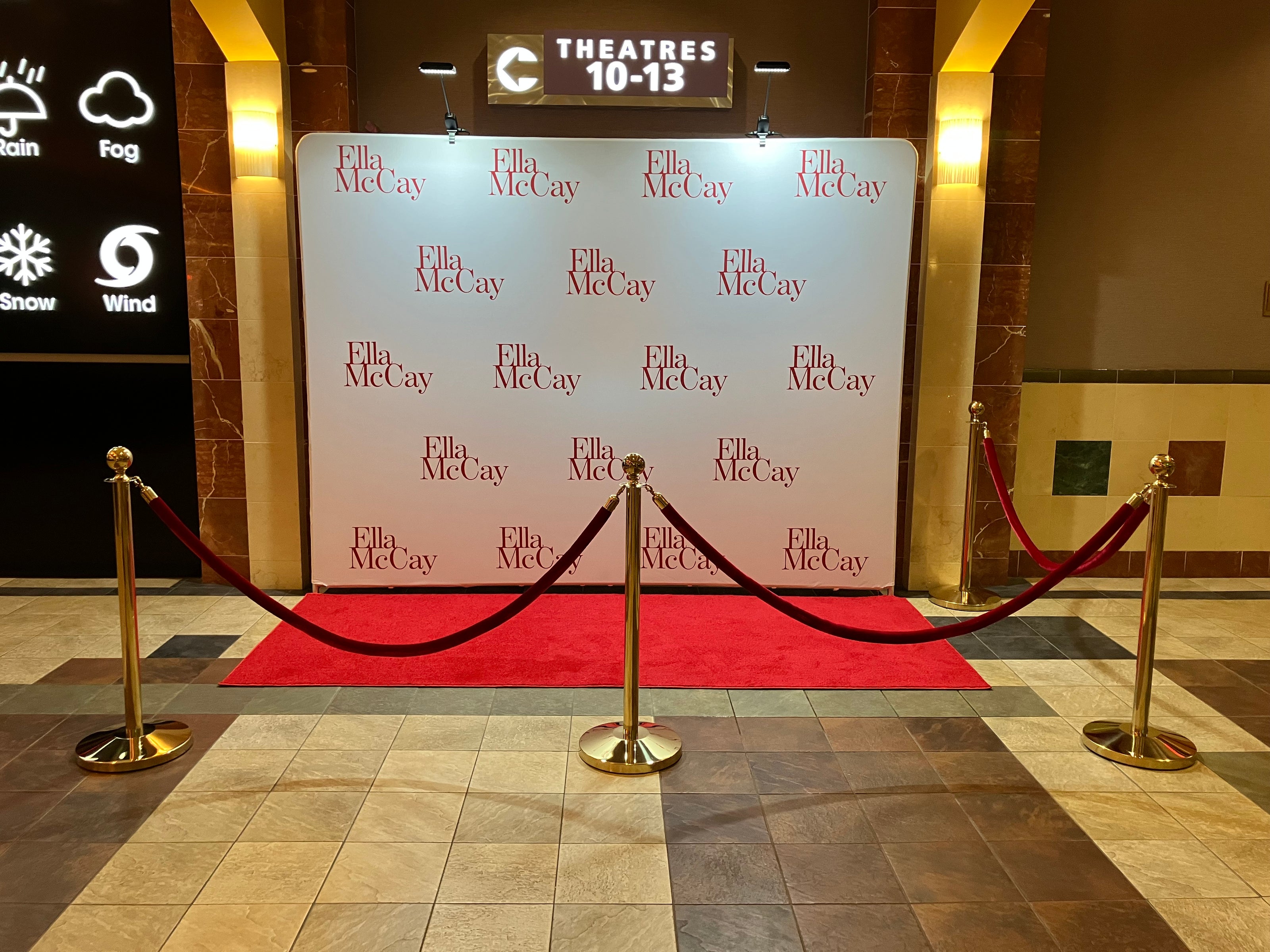 Red carpet event setup with 'Ella McCay' step and repeat tension banner branding at a theater entrance.