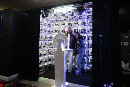Two people standing inside an immersive cube with a large display of foil balloons and an open-air photo booth.