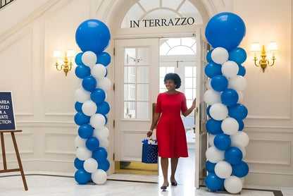 Blue and white balloon columns flanking a doorway with beautiful black woman walking through.